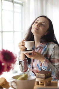 快乐的女孩手里拿着一杯香咖啡。好的早餐在家在客厅在窗口。文本的可用空间