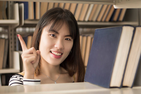 聪明女大学生找书女大学生快乐微笑的肖像在图书馆里找书或课本, 指着一根手指亚洲年轻的成年妇女模型