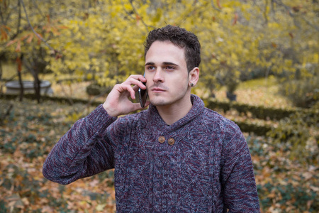 严肃的年轻英俊的人在一个公园讲电话在秋天
