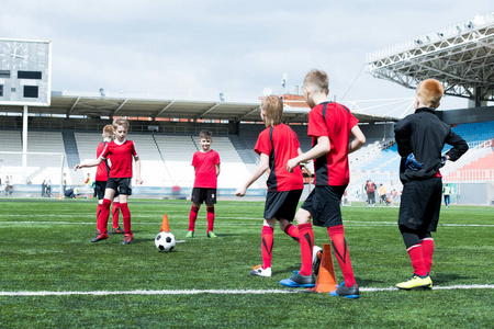 少年足球队的全长画像在体育场练习, 男孩带领球在橙色锥体之间, 拷贝空间