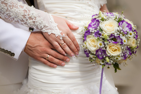 新娘和新郎的手的婚礼花束和环