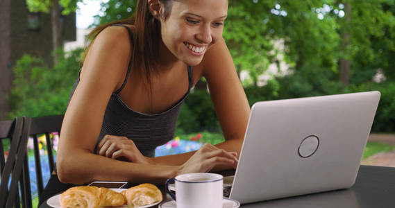 漂亮的白人妇女在户外浏览笔记本电脑时吃早餐