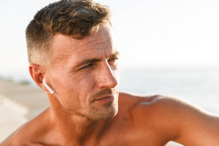 在海滩上关闭英俊的无上衣的运动员与耳机