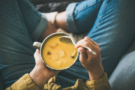 扁平的女性在黄色衬衫坐保持杯的秋天温暖南瓜奶油汤与面包丁, 顶部视图。秋季素食, 素食主义者, 健康舒适饮食概念