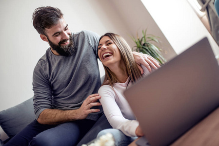 年轻幸福夫妇坐在沙发上, 使用笔记本电脑在线购物在客厅