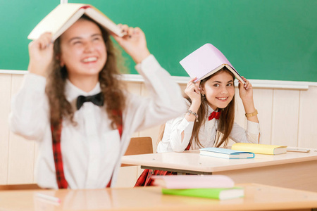 学校校服的女生们在教室里坐着情侣。女孩上学。在教室里的女生读书籍和使用智能手机