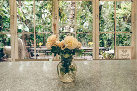 一张玫瑰花瓶, 桌上有花园风景的玻璃屋