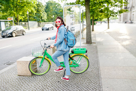 现代妇女穿着休闲服装使用出租和共享系统在城市街道使用电动自行车或电子自行车
