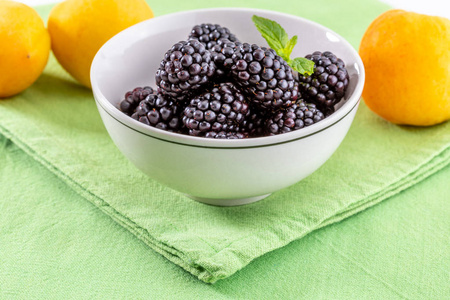 美味的新鲜黑莓和成熟的黑色和红色石榴石。在白色碗在绿色和白色背景。与杏