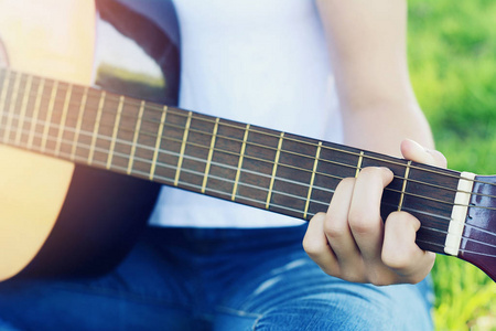 特写的年轻女子手玩声学吉他在公园