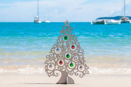 木圣诞树与装饰站立在海岸与白色沙子, 清澈的蓝色水和游艇远在普吉岛, 泰国假日和在热带地区的假期的概念