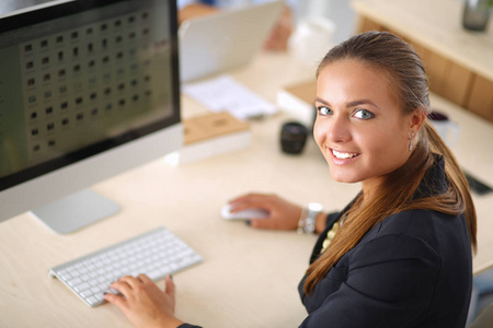 年轻女子在办公室工作，坐在办公桌前，使用笔记本电脑