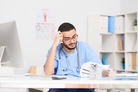 青年中东医生戴眼镜坐在办公室和阅读病人报告的纵向