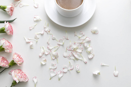 白杯中的咖啡, 粉红色和白色康乃馨花和花瓣在白色的桌子上。顶部视图