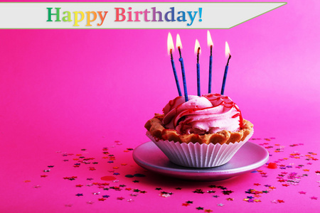生日杯蛋糕蜡烛与粉红色的背景上五颜六色的星星