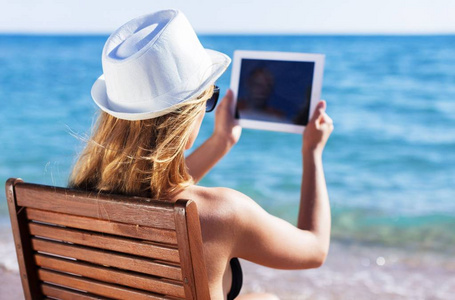 年轻女子在 tablet pc，在海滩的帽子