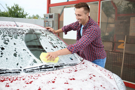 青年男子清洁车与海绵在自助式洗车服务