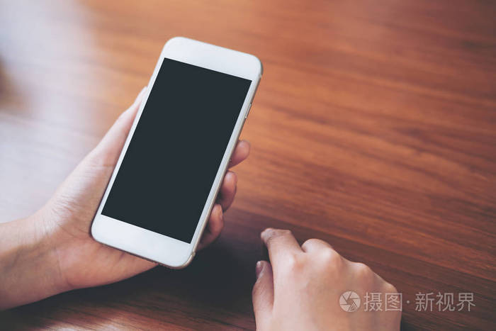 老式木桌上手持空白黑屏手持白色手机的样机图像