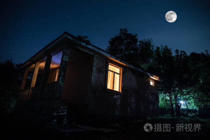 晚上在森林里建筑的山夜风景与月亮或老式乡下房子在晚上与云彩和星