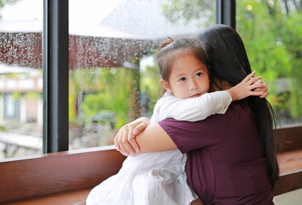 在雨天, 亚洲母亲和女儿抱着爱在玻璃窗边拥抱