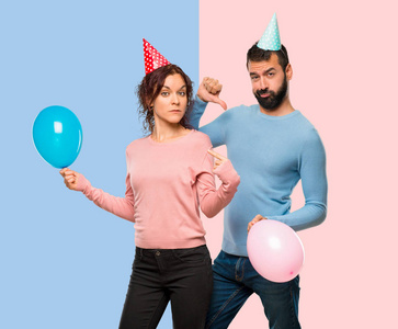 一对夫妇与气球和生日帽骄傲和自鸣得意, 在爱自己的概念在粉红色和蓝色的背景