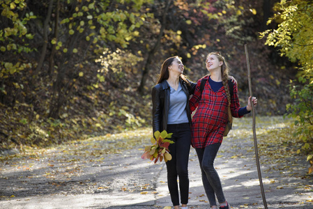 两个笑着的女人在公园里散步。秋天森林在距离
