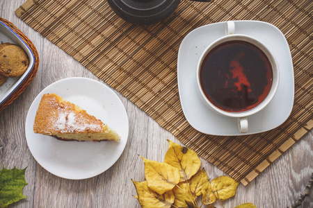 一个老茶壶在稻草床上用品与一杯热茶一块李子海绵蛋糕和巧克力曲奇饼干的背景下, 秋叶