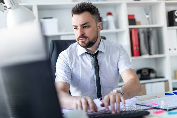 一个男人坐在办公室的桌子旁, 用文件和电脑工作.
