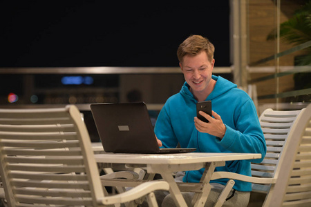 晚上在户外使用手机和笔记本电脑的快乐男人
