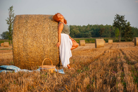 红头发的女人在干草堆附近的田野上摆姿势