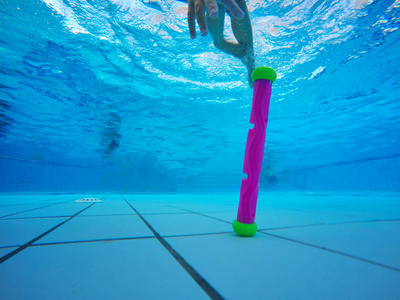体育小女孩潜水到池底, 并收集在蓝色背景的玩具。在水下射击