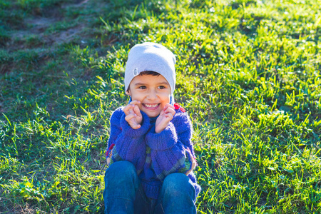 愉快的男孩在帽子和毛衣坐在草地上
