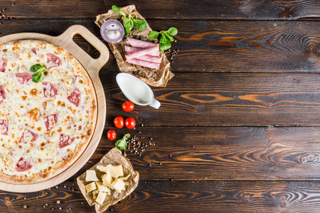 大比萨饼与火腿和蘑菇在一个圆形的切菜板上的一个黑暗的木制背景。披萨配料