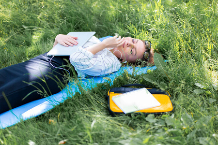 妇女休息在公园躺在草地上的笔记本电脑和听音乐