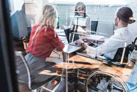 透过轮椅的年轻残疾商人在办公室与同事合作
