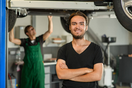 一个穿着黑色 t恤衫的年轻英俊的家伙在一个工作机械师的背景下拍照。