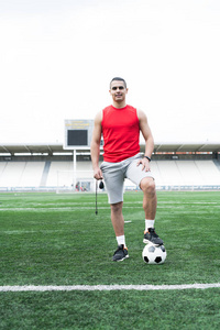 英俊的拉丁美洲男子的全长肖像在体育场里摆着足球, 看着相机愉快地微笑着, 复制空间