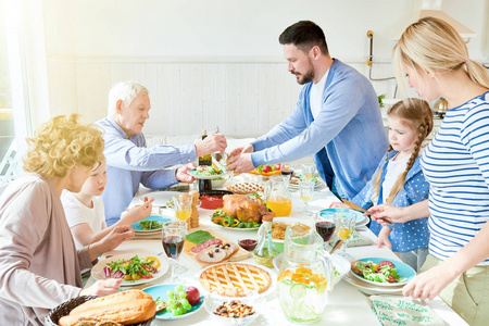 在阳光照射下的现代公寓里, 两个大的两代家庭在节日庆祝活动中, 一起坐在节日的桌旁, 吃着美味的菜肴