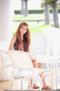 亚洲微笑的年轻女子坐在现代白色椅子上，放松