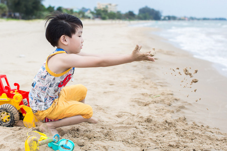 在海滩上的小亚洲男孩玩沙