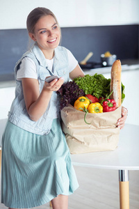 年轻女子捧着蔬菜杂货店购物袋。站在厨房