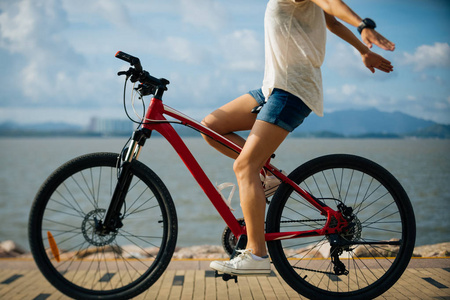 自由妇女骑自行车在阳光明媚的海滨伸出双臂