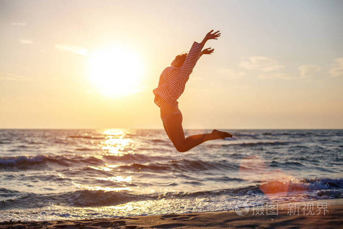 快乐自由的女人在夕阳下的沙滩上快乐的跳跃着