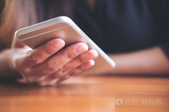 在办公室的木桌上手持和使用智能手机的女性特写图像