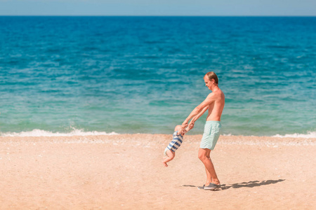 年轻快乐的父亲在沙滩上和他的孩子玩耍。婴儿转过身, 旋转着