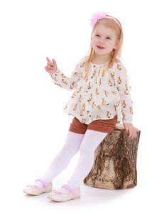 小女孩穿着短裤坐在一个树桩