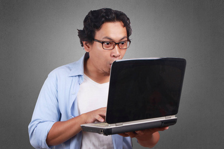 年轻的亚裔男子身穿白色和蓝色衬衫感到惊讶, 在笔记本电脑上的新闻震惊。关闭正文肖像