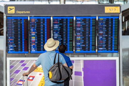 旅客的背面与行李站在航班板上办理登机手续在现代机场的航班信息屏幕上, 旅行和运输与技术概念