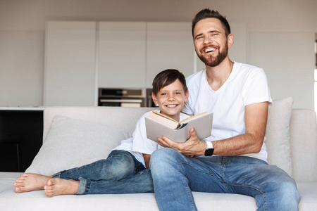 一个快乐的年轻父亲和他的儿子的肖像在家里玩的时候一起看书