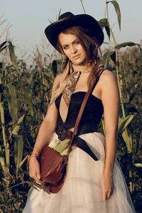 一位身着牛仔服装的年轻女子在日落时站在农夫的麦田地里, 在干草堆里休息。